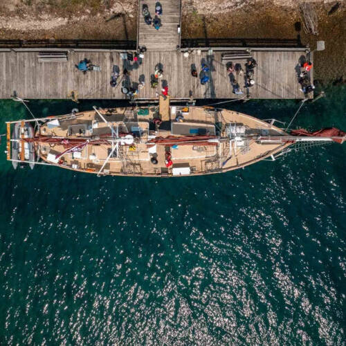 Aerial view of a sailboat docked at a pier with people on it, set in clear turquoise water.
